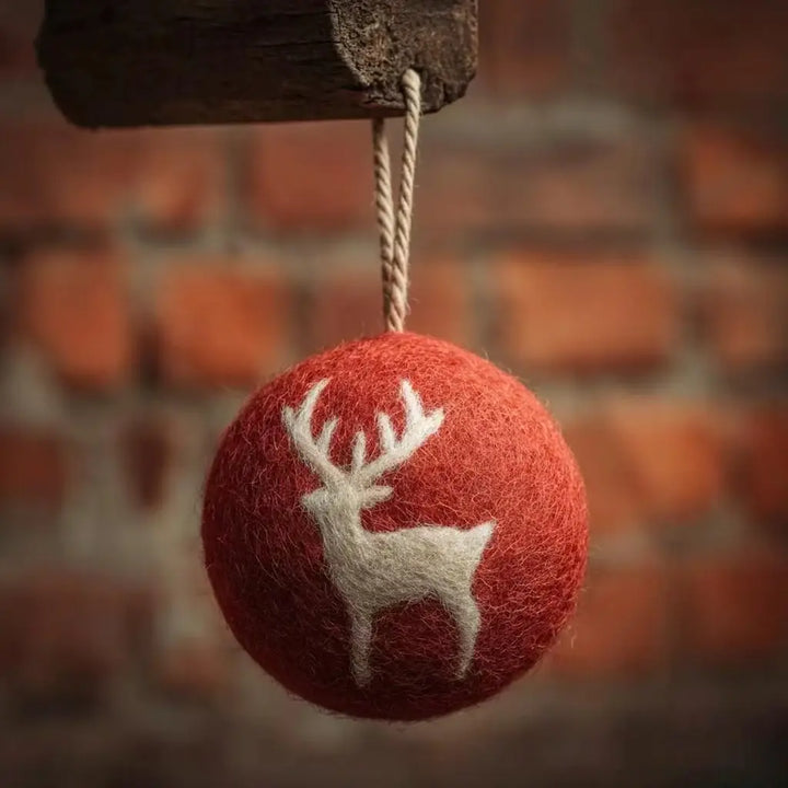 Red ornament with a white deer design hanging against a brick wall.