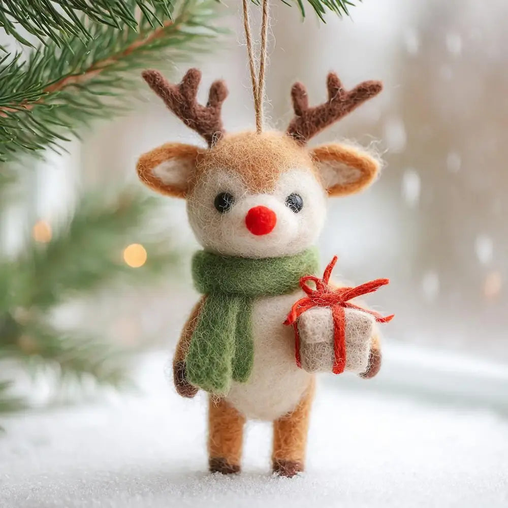Felt reindeer ornament with a green scarf and red nose, holding a small gift, against a snowy background.