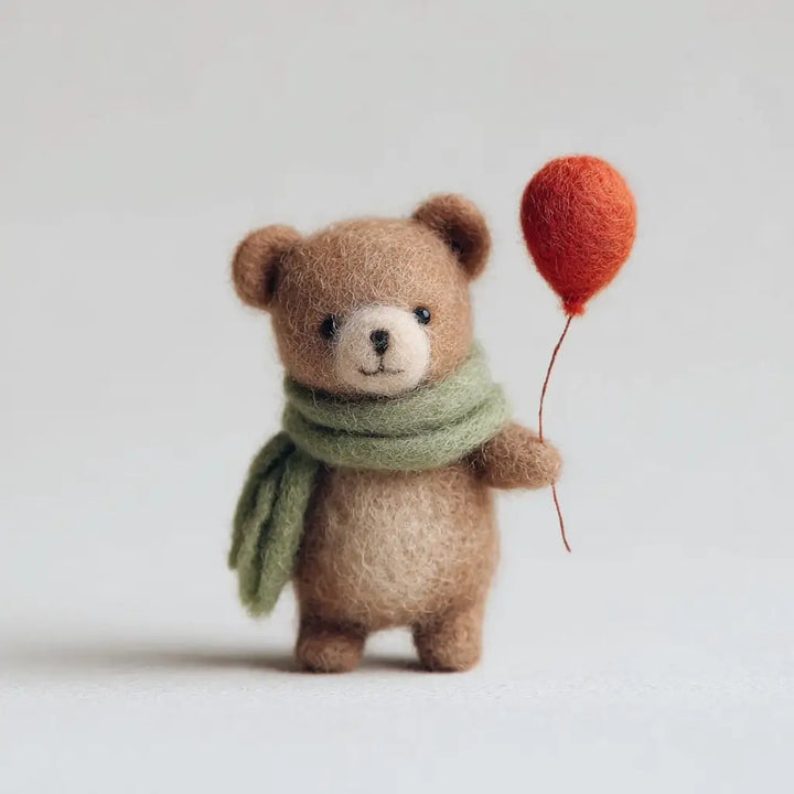 Small brown teddy bear with a green scarf and red balloon on a light background