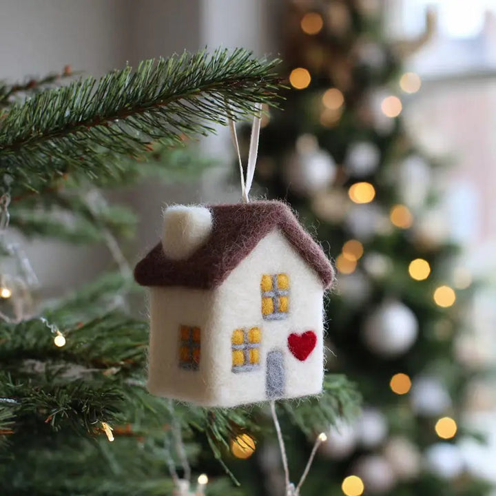 Decorative house ornament hanging on a Christmas tree with blurred lights in the background