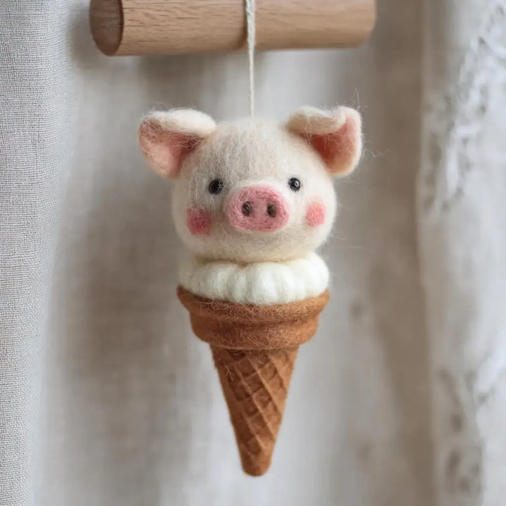 Felted pig toy in an ice cream cone against a neutral background