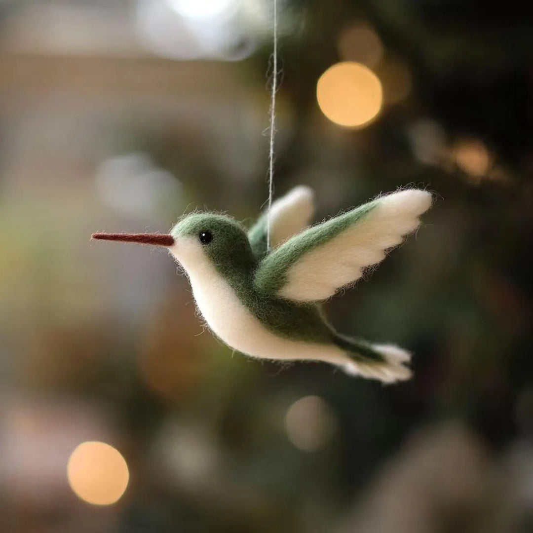 Felted hummingbird ornament hanging against a blurred natural background