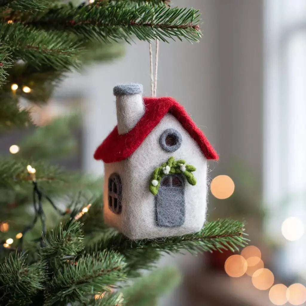 Felt house ornament with a red roof hanging on a Christmas tree.