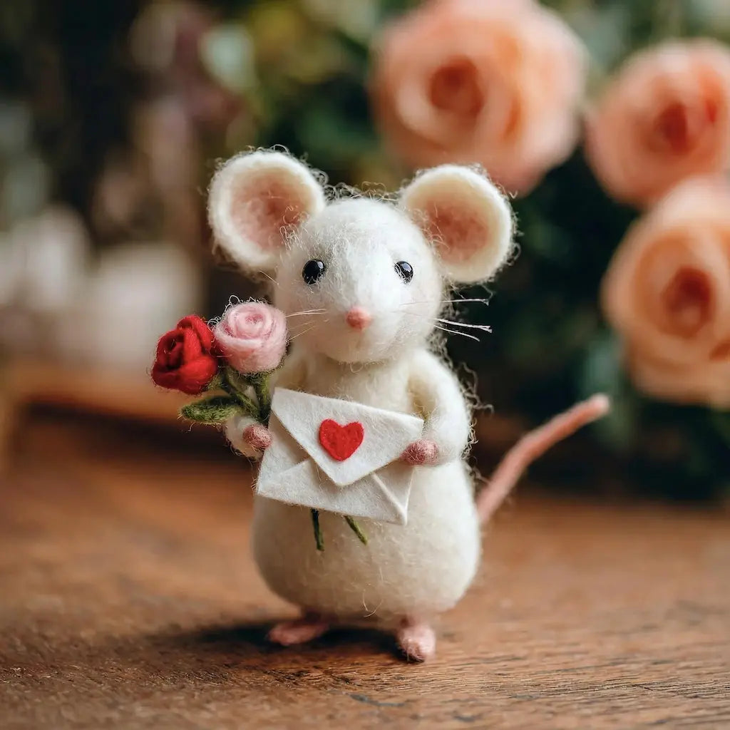 Stuffed mouse holding flowers and a letter with a heart on a wooden surface.