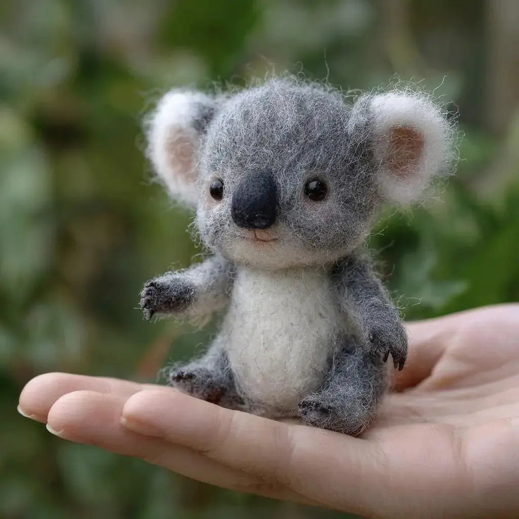 Small felted koala toy held in a hand with a blurred green background
