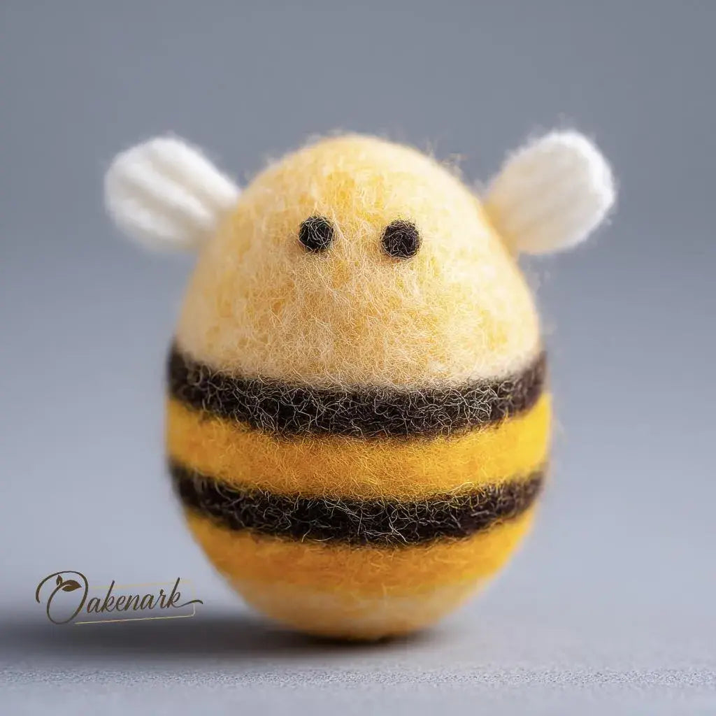 Felted bee-shaped object with black stripes on a gray background, featuring the brand 'Oakenark'.