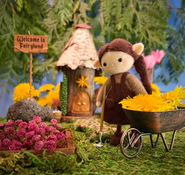 Fairy garden scene with a fairy doll, flower cart, and miniature house.