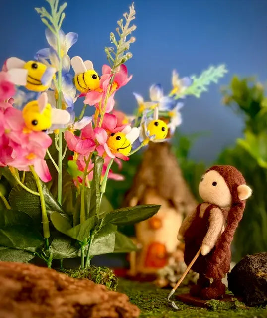 Small monkey figurine next to colorful flowers and butterflies in a forest setting