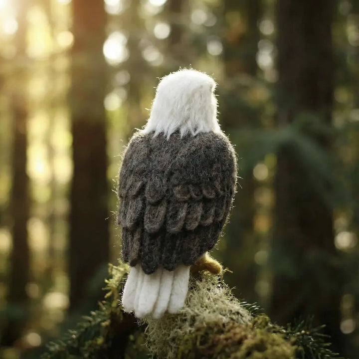 Felted eagle toy on a branch with a forest background