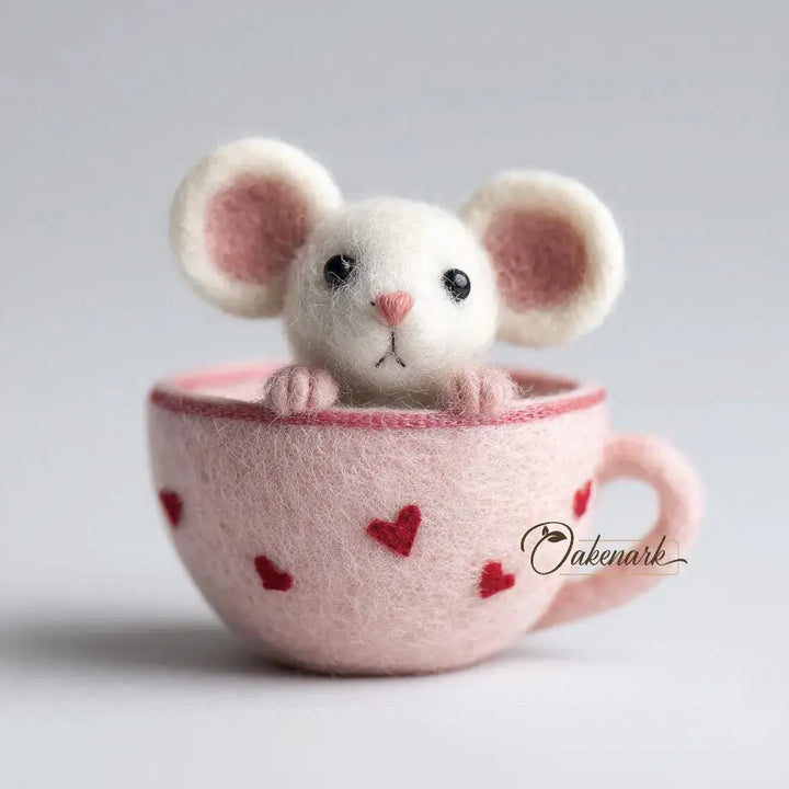 White mouse plush toy inside a pink teacup with heart patterns on a light gray background.