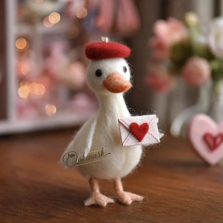 Decorative figurine of a bird holding a heart-shaped letter on a wooden surface with blurred lights and flowers in the background.