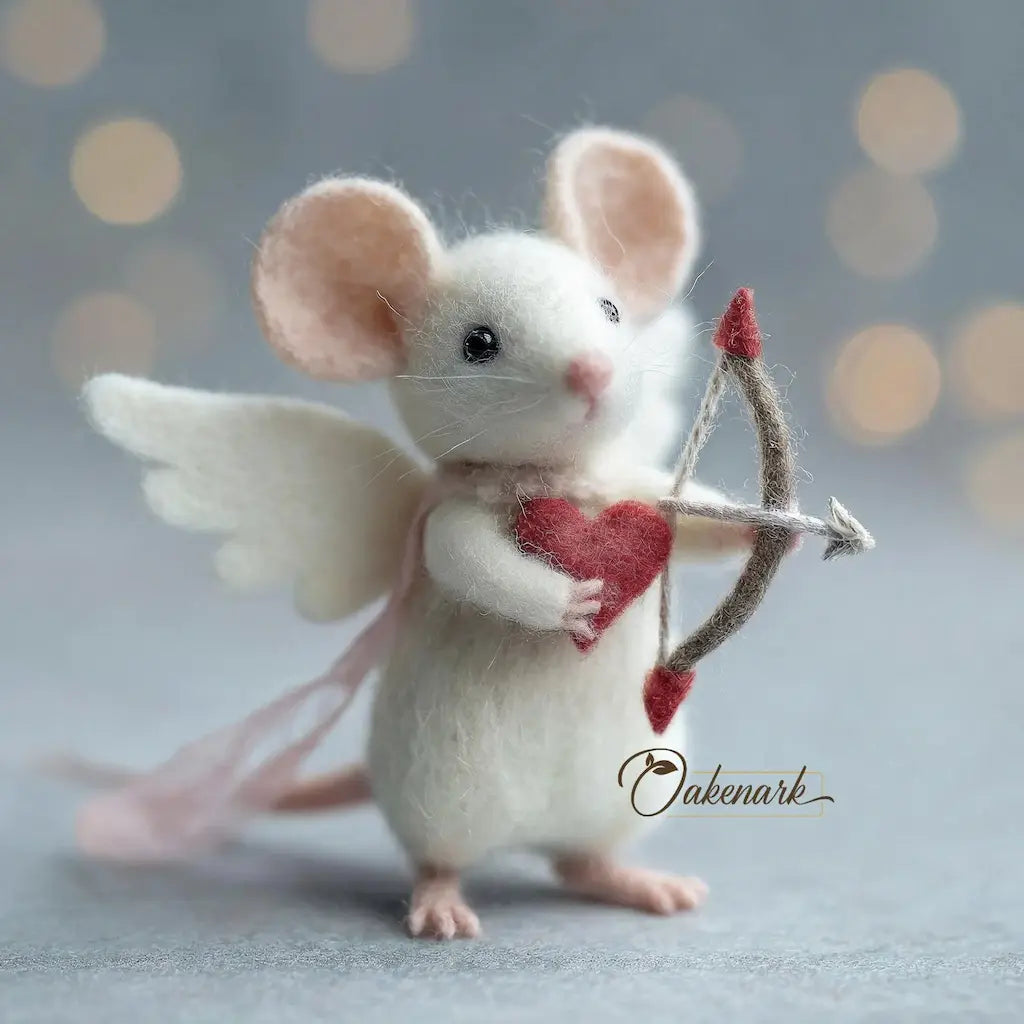 Felted mouse with angel wings and a bow, holding a heart, on a soft gray background.