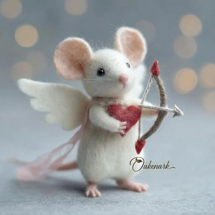 Felted mouse with angel wings and a bow, holding a heart, on a soft gray background.