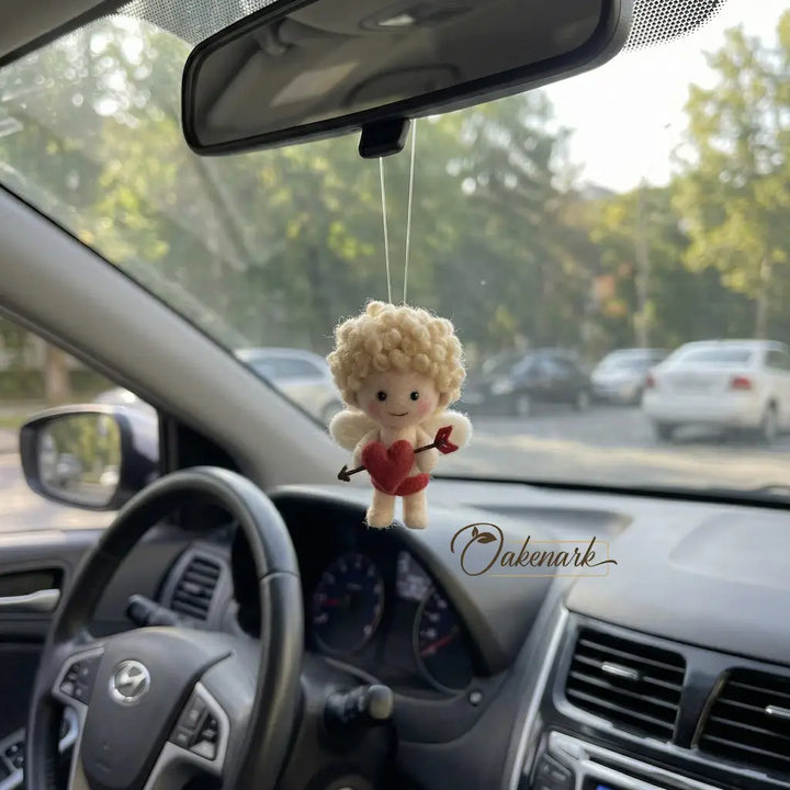 Car interior with a plush toy angel hanging from the rearview mirror, branded &