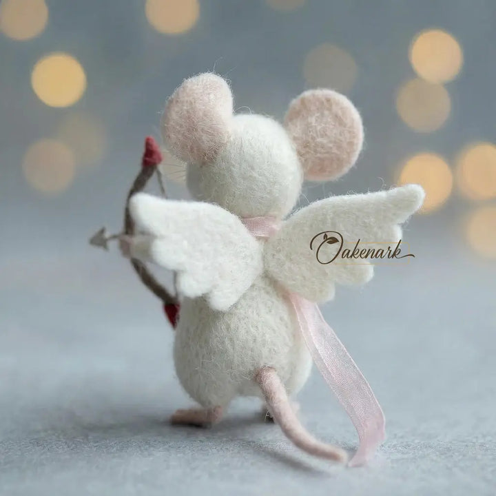 White mouse figurine with angel wings and a bow, on a soft gray background with blurred lights.