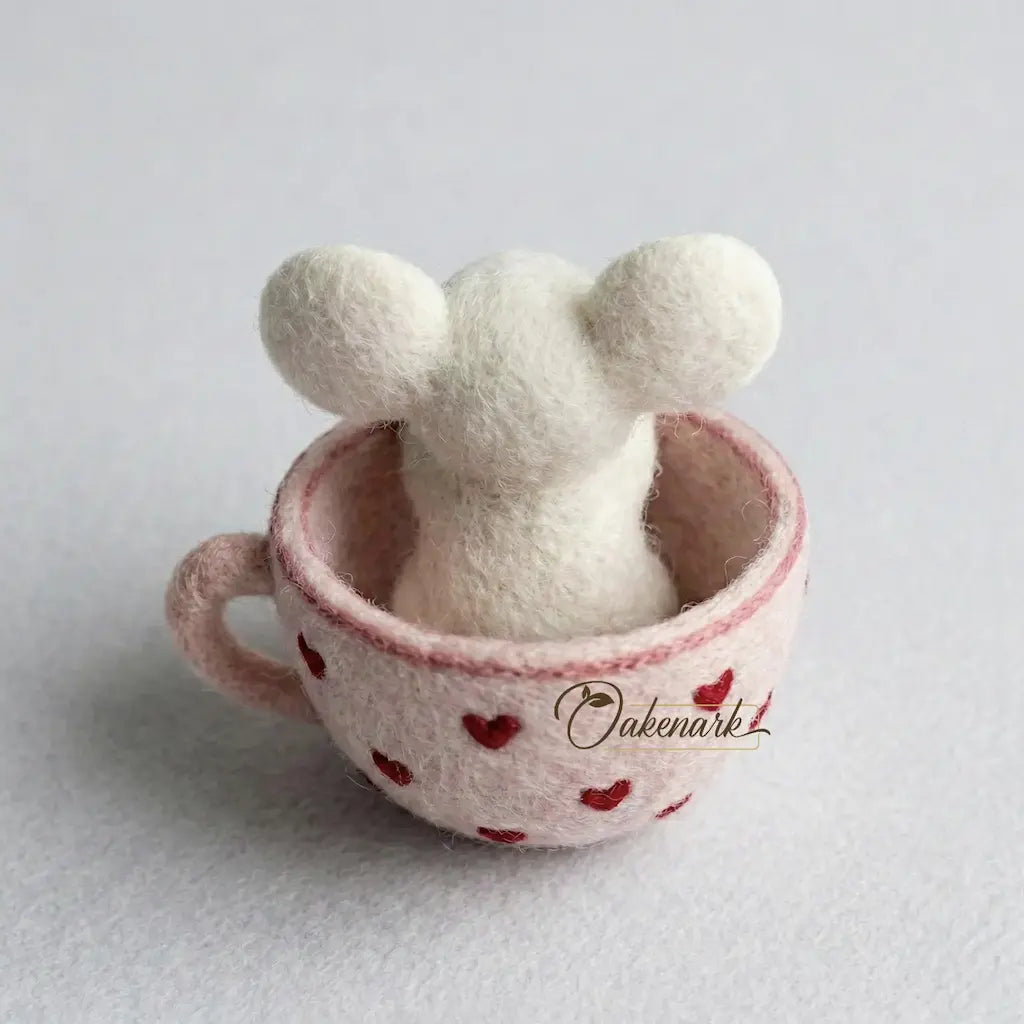 White plush toy with ears in a pink cup with red heart pattern on a light gray background
