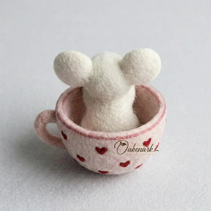 White plush toy with ears in a pink cup with red heart pattern on a light gray background