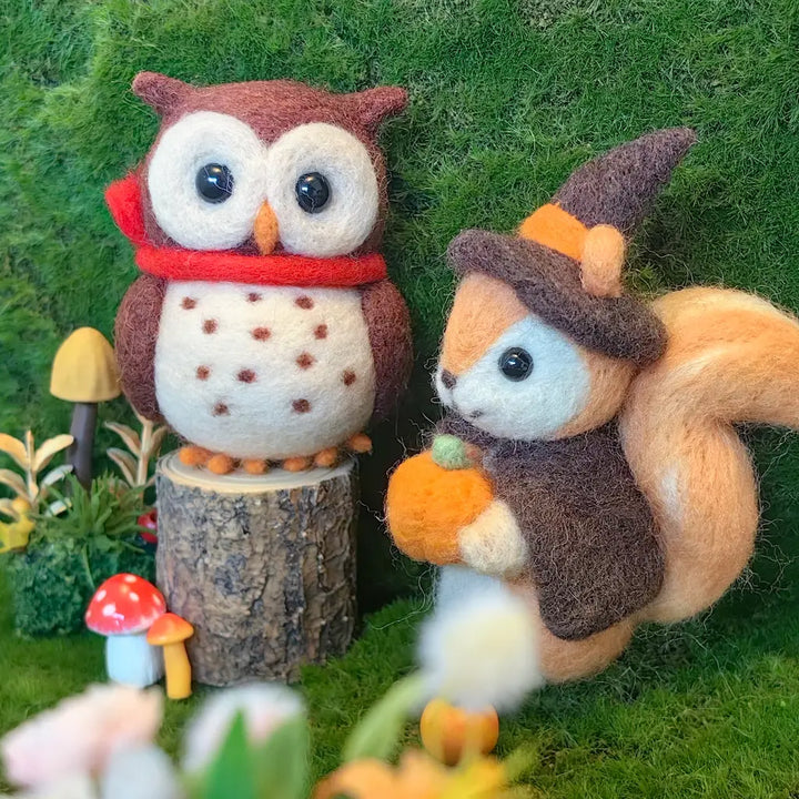 A felt needle art decoration set featuring a brown owl wearing a red scarf and a brown squirrel wearing an autumn witch hat and brown cape, holding a pumpkin, set against a green moss background with miniature mushrooms.