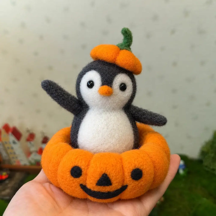 Pumpkin Parade penguin figurine held in an open palm, showing the wool texture, pumpkin cap and smiling pumpkin costume.
