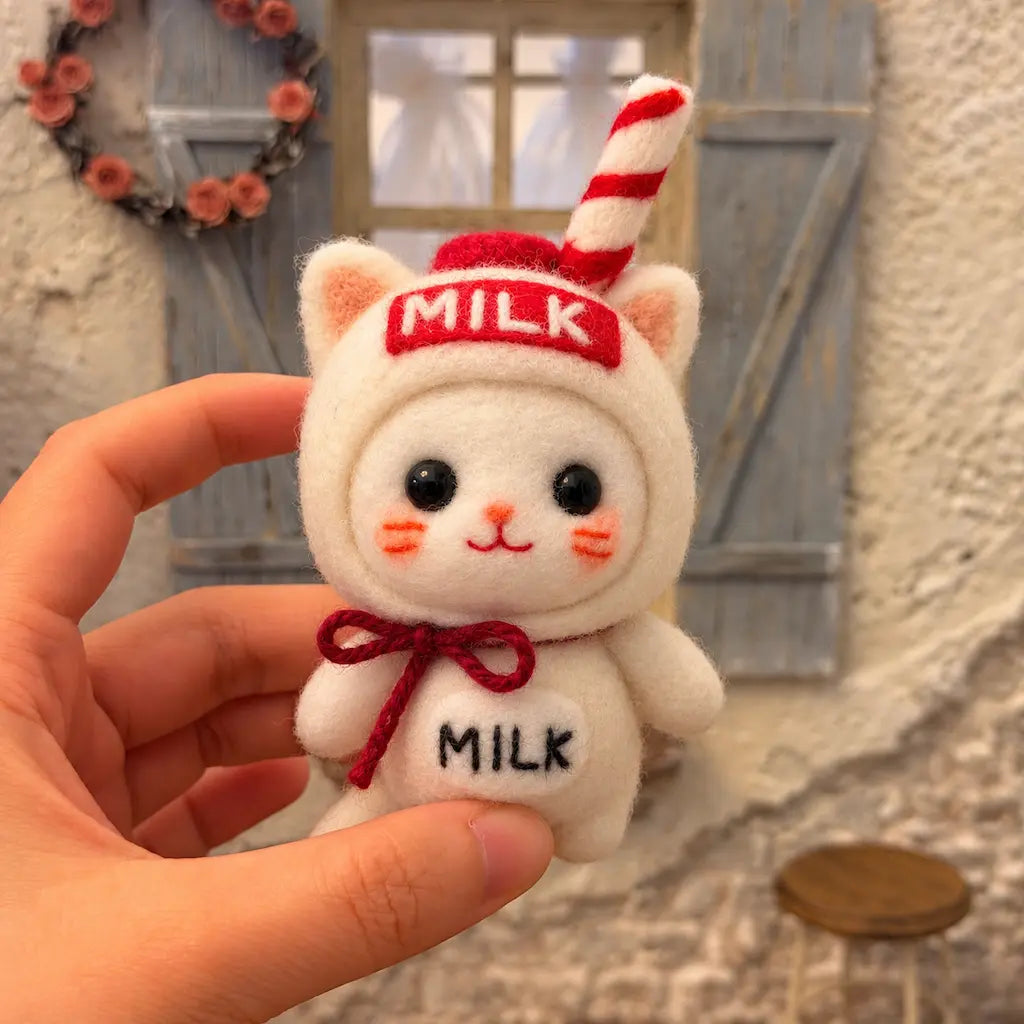Milk Carton Cat felt figurine held in one hand in front of a blue-shuttered window, showing the full striped straw.