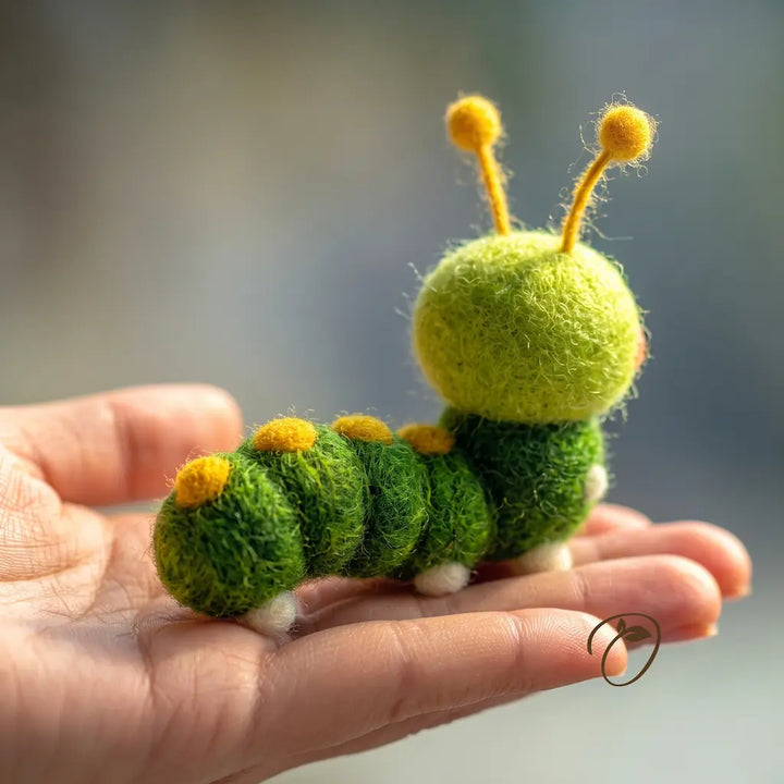 A small felted wool caterpillar toy in shades of green and yellow, resting on a person&