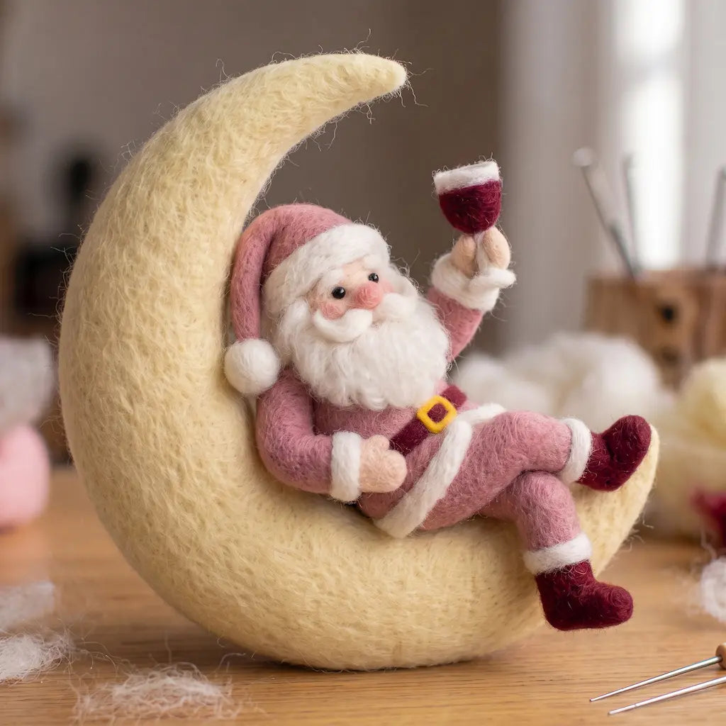 Pink wool felt Santa reclining on a cream crescent moon, raising a burgundy goblet with his legs crossed.