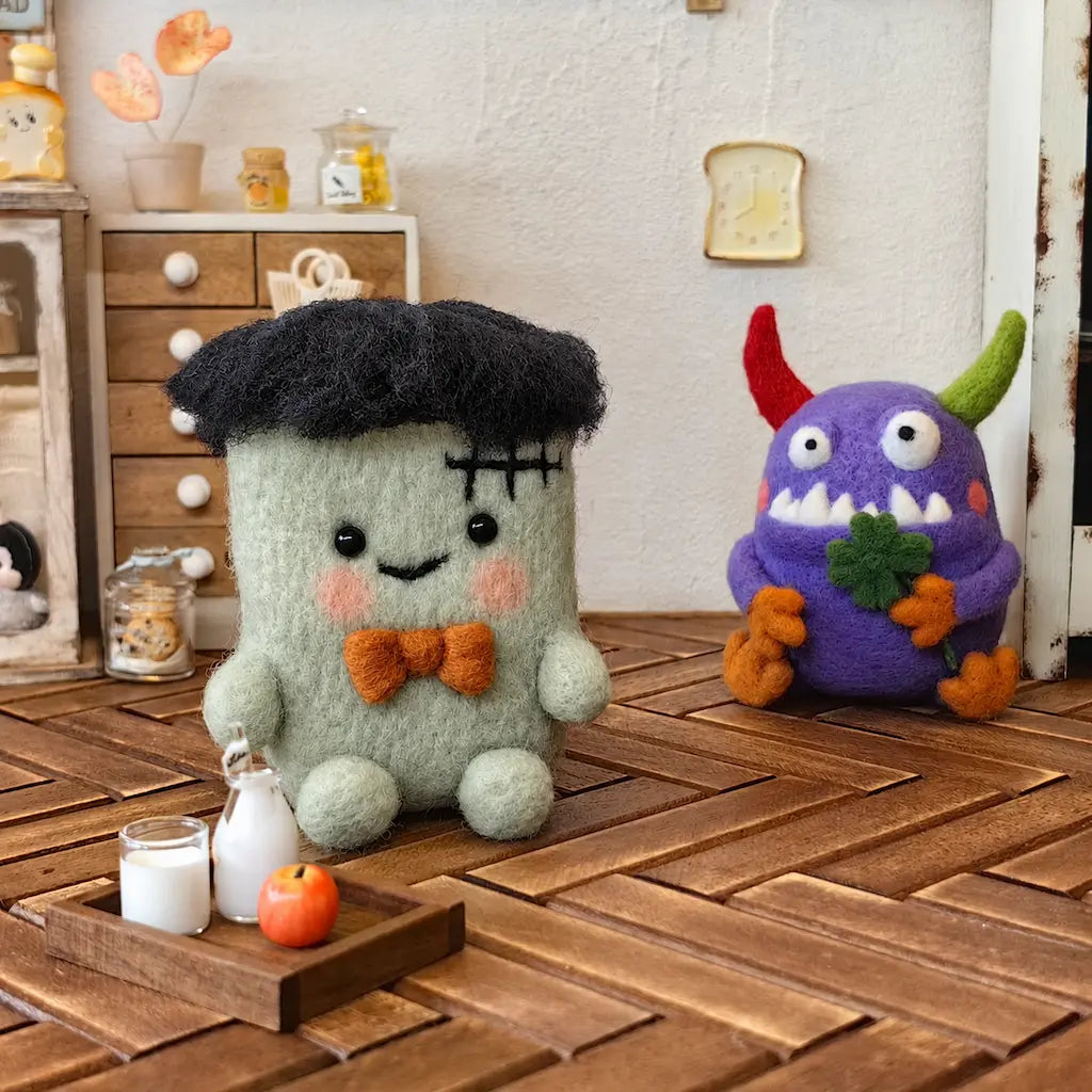 Two colorful felt monster characters displayed in a miniature kitchen scene.