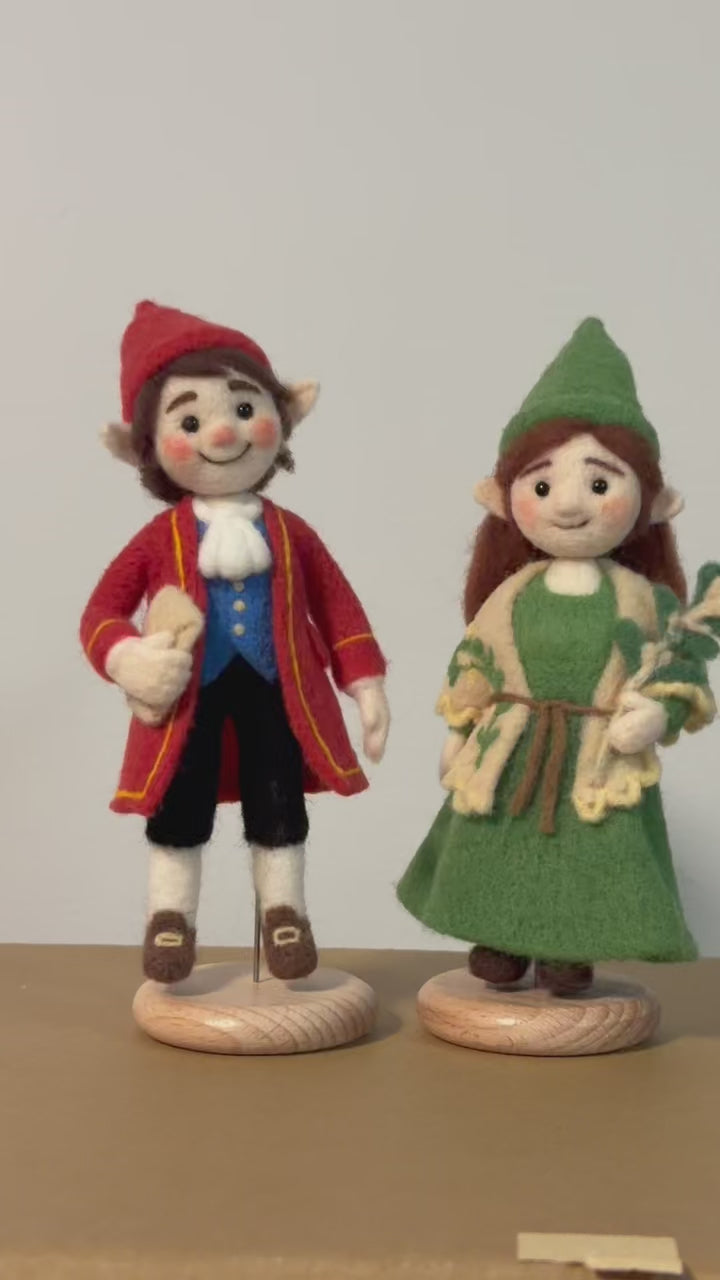 Two felted figurines, one in a red outfit and the other in a green outfit, on a plain background.