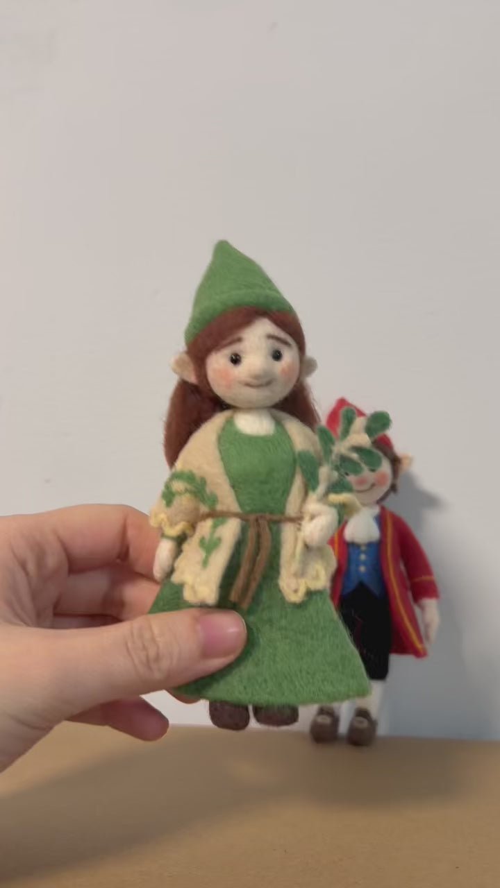 Two felted figurines, one in a red outfit and the other in a green outfit, on a plain background.