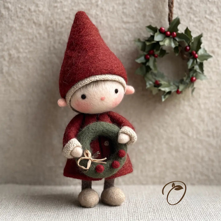 A handmade felt Christmas gnome ornament wearing a red hat and coat, holding a green wreath with red berries, standing on a textured beige surface with a matching holly wreath hanging in the background.