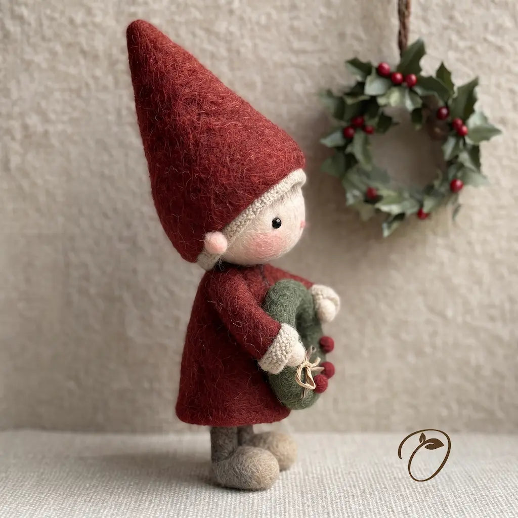 A handcrafted felt Christmas gnome ornament wearing a tall burgundy hat and coat, holding a green wreath with red berries, set against a neutral textured background with a holly wreath hanging in the background.