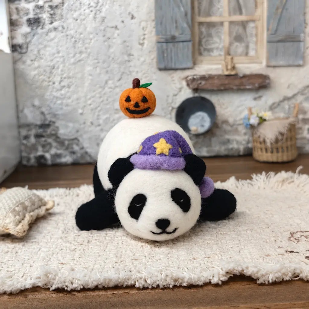 Front view of the Sleepy Panda with Pumpkin felt figurine lying peacefully with its head on its paws, wearing a purple sleeping cap beneath a tiny Halloween pumpkin.