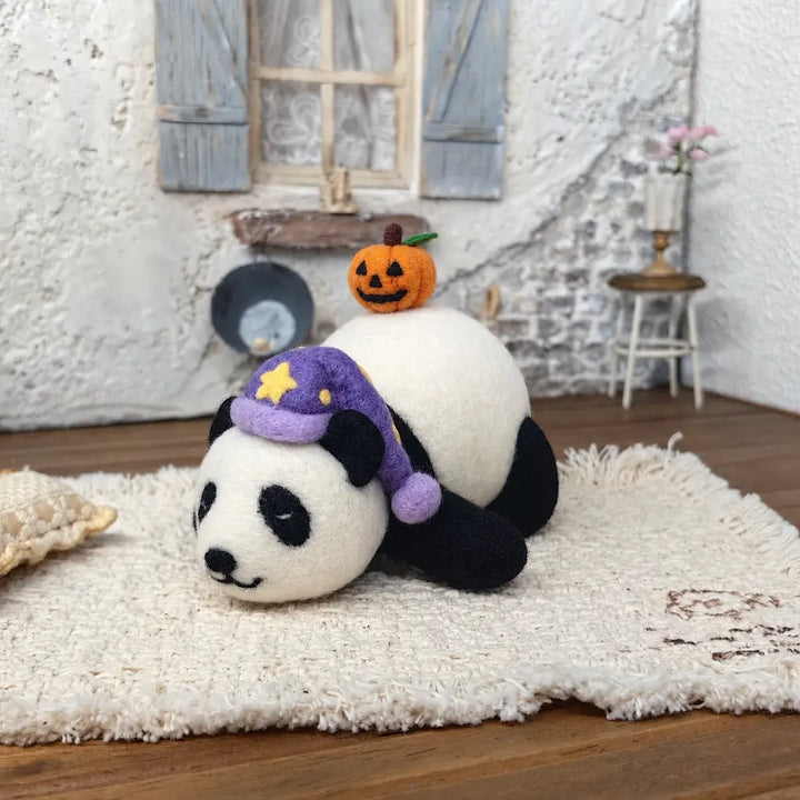 Side view of a sleeping needle-felted panda with closed eyes, black-and-white wool body, purple nightcap with yellow stars and a small pumpkin on its back.
