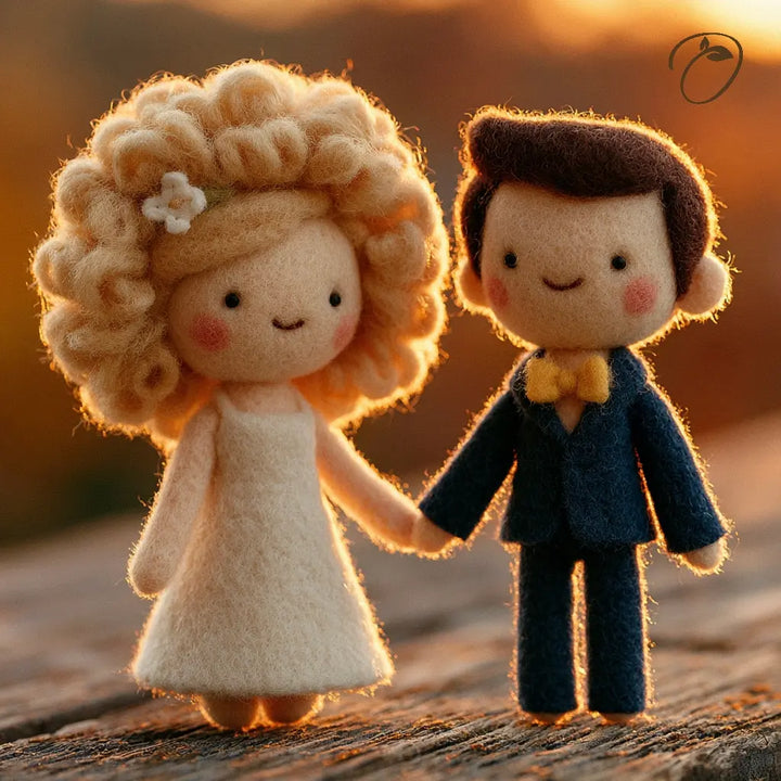 Two cute felt doll figurines holding hands, with a bride-like doll in a cream dress and a groom-like doll in a navy suit with a yellow bow tie, set against a warm sunset background.