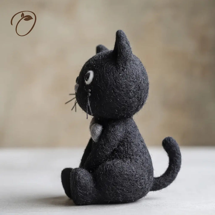 Side view of Wide Eyed Black Cat felt figurine showing its grey bow tie, fine whiskers, seated paws and upward-curved tail