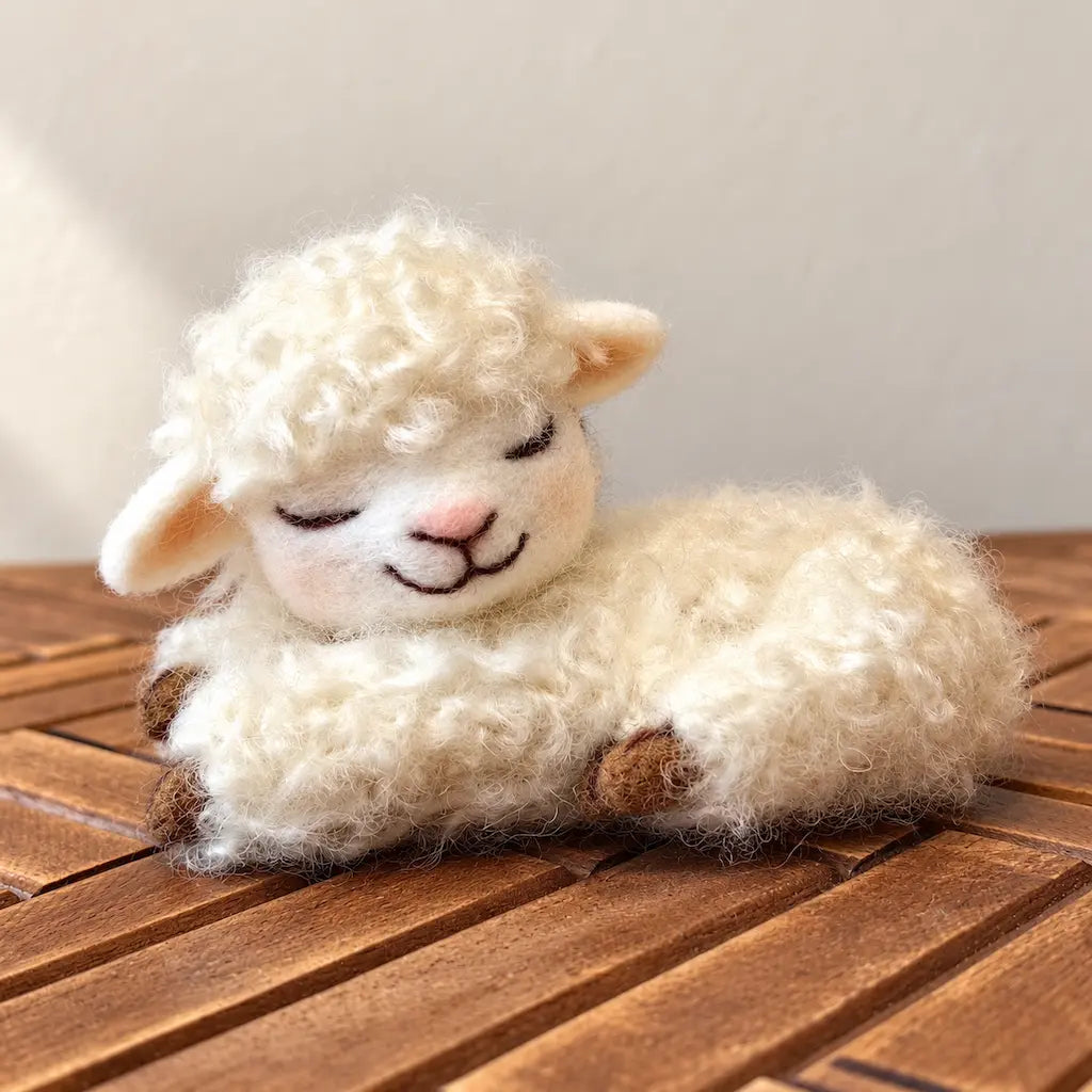 Curly fleece sleeping lamb felt figurine resting on wooden slats, with closed eyes, cream-colored curls, and a small smile.